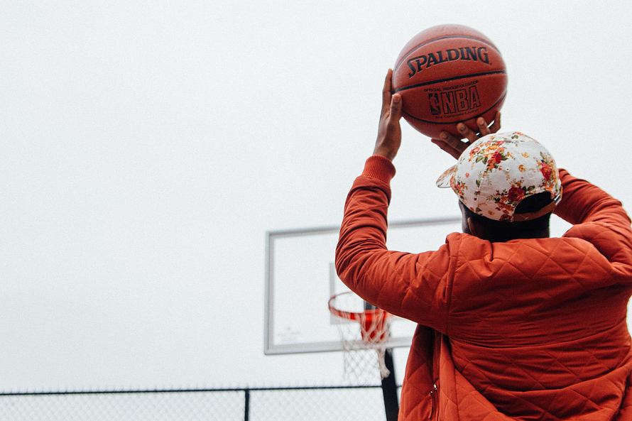Dating Tips: Learn sports. Man wearing an orange jacket, shooting a basketball.