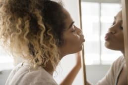 African American woman with curly hair promoting self-love by kissing herself in a mirror