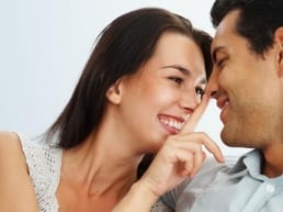 woman flirting before sex, with man. Woman has her finger on the man's nose as he smiles.