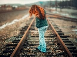Red Haired Woman sad about her relationships, standing on the train tracks because the pain of her relationships are unbearable