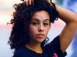African American woman with freckles that Typically carries a label holding her head full of curly hair in a pose