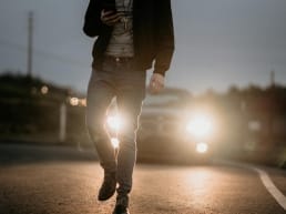 man walking on a road looking at his cell phone distracted with a car approaching from behind