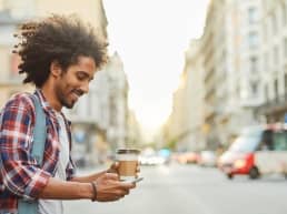 You African American man with curly hair, holding a coffee, in a textationship on the the go, messaging a woman with a woman