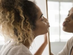 African American woman with curly hair promoting self-love by kissing herself in a mirror
